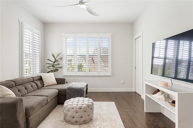 living room featuring dark wood-type flooring, baseboards, ceiling fan, and a healthy amount of sunlight
