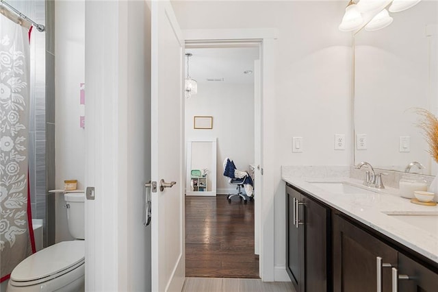 full bathroom with double vanity, wood finished floors, a sink, baseboards, and toilet