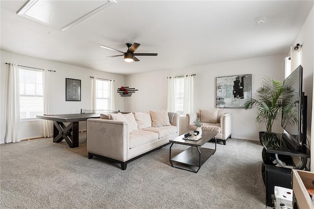 carpeted living area featuring baseboards, a ceiling fan, and attic access