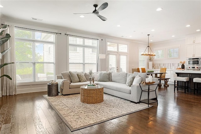 living area with ornamental molding, a ceiling fan, dark wood finished floors, and visible vents