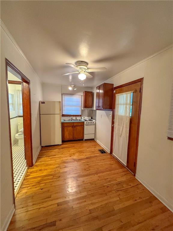 kitchen featuring white appliances, ceiling fan, crown molding, sink, and light hardwood / wood-style floors