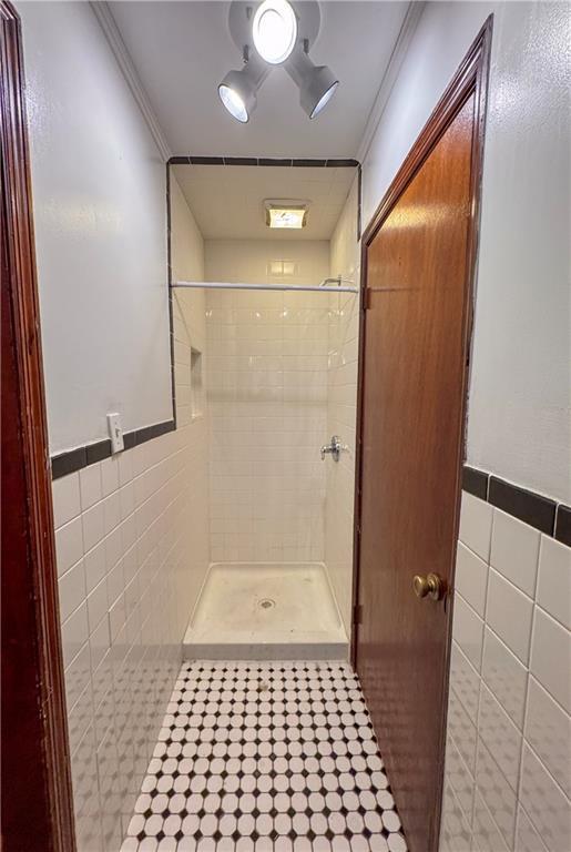 bathroom with a tile shower, tile walls, and ornamental molding