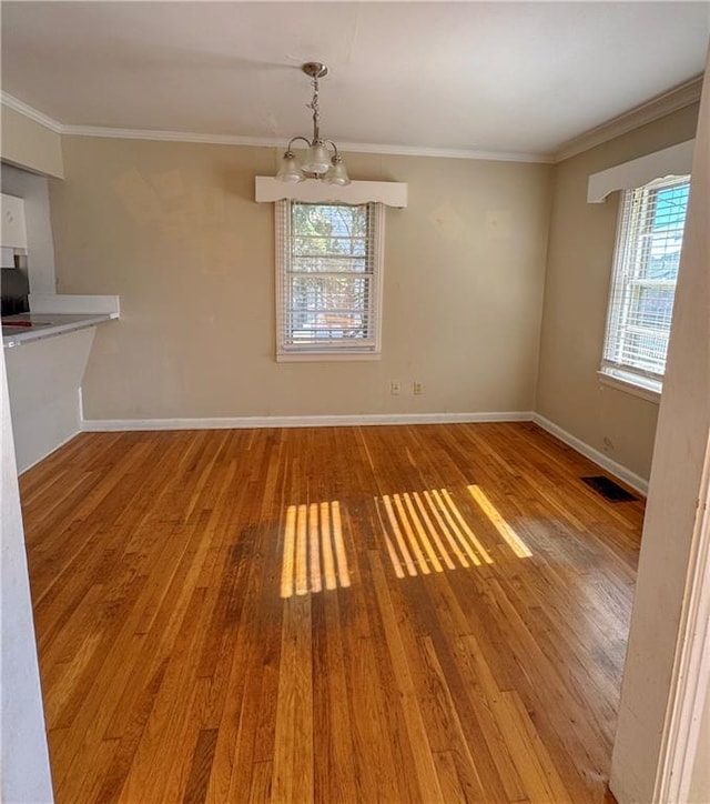 unfurnished dining area with a wealth of natural light, hardwood / wood-style floors, ornamental molding, and a notable chandelier