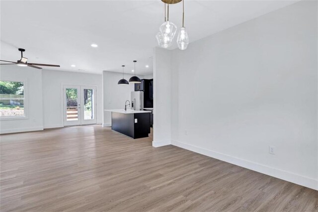 unfurnished living room featuring light hardwood / wood-style floors, sink, ceiling fan, and french doors