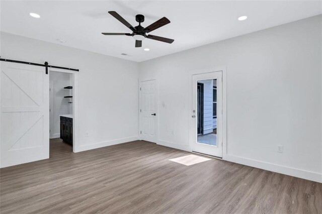 unfurnished bedroom featuring access to outside, a barn door, ceiling fan, hardwood / wood-style floors, and ensuite bath