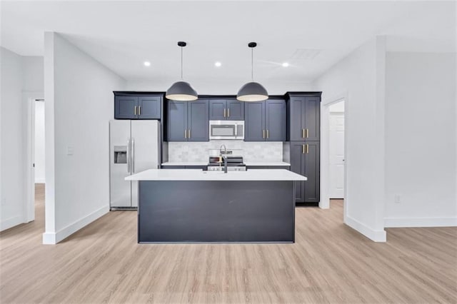 kitchen with tasteful backsplash, stainless steel appliances, light hardwood / wood-style floors, pendant lighting, and a center island with sink