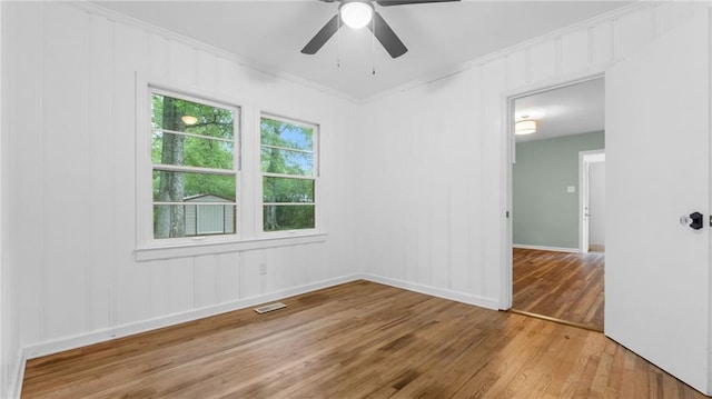 empty room with light wood-style flooring, crown molding, ceiling fan, baseboards, and a decorative wall