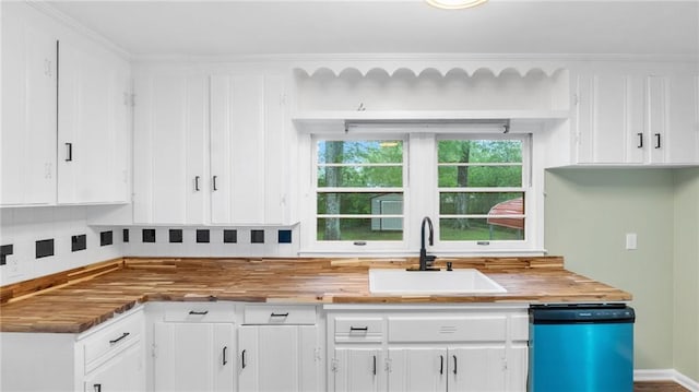 kitchen with dishwashing machine, a sink, wood counters, and white cabinets