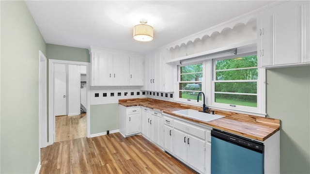 kitchen with dishwashing machine, a sink, wood counters, and white cabinets