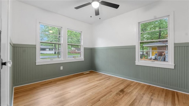 empty room featuring wainscoting, wood finished floors, and ceiling fan