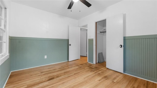 unfurnished bedroom featuring a wainscoted wall, wood finished floors, a closet, and a ceiling fan
