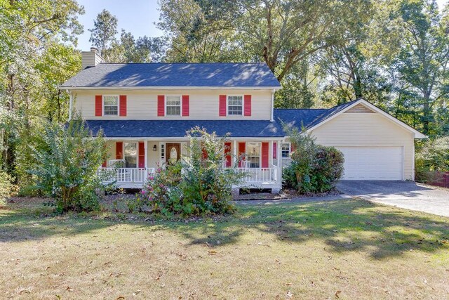 view of front of property featuring covered porch, a garage, and a front lawn