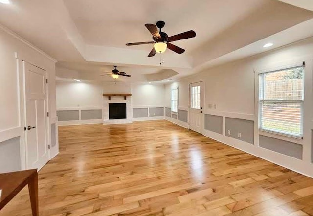 unfurnished living room with ceiling fan, plenty of natural light, a raised ceiling, and light wood-type flooring