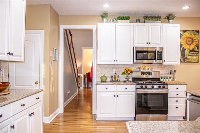 kitchen featuring backsplash, light hardwood / wood-style flooring, light stone countertops, appliances with stainless steel finishes, and white cabinetry