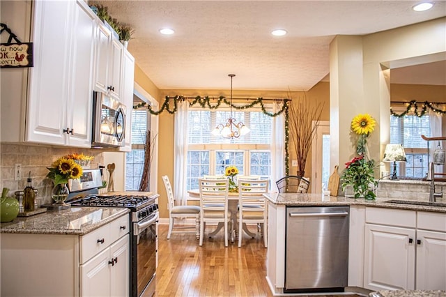 kitchen featuring white cabinetry, sink, hanging light fixtures, kitchen peninsula, and appliances with stainless steel finishes