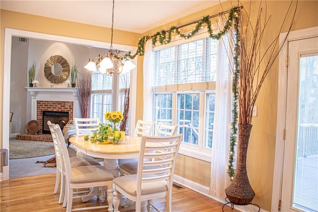 dining area with an inviting chandelier, light wood-type flooring, and a brick fireplace