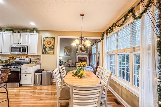 dining room with a fireplace, a textured ceiling, an inviting chandelier, and light hardwood / wood-style flooring