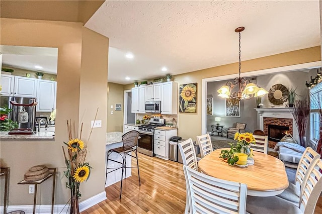 dining room with a chandelier, a textured ceiling, light wood-type flooring, and a brick fireplace