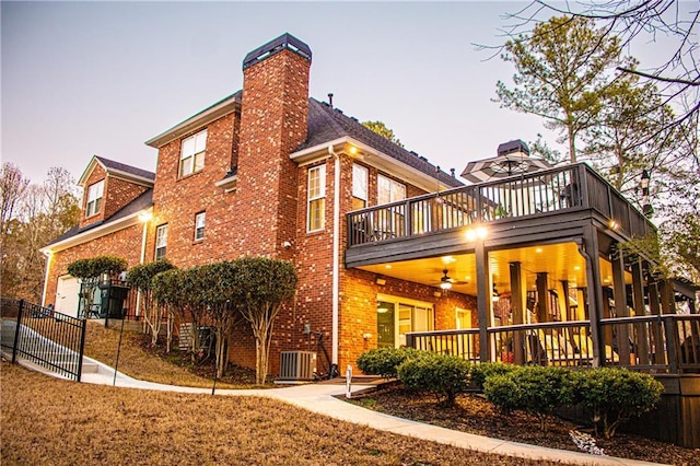 back house at dusk with ceiling fan, a balcony, central AC unit, and a garage