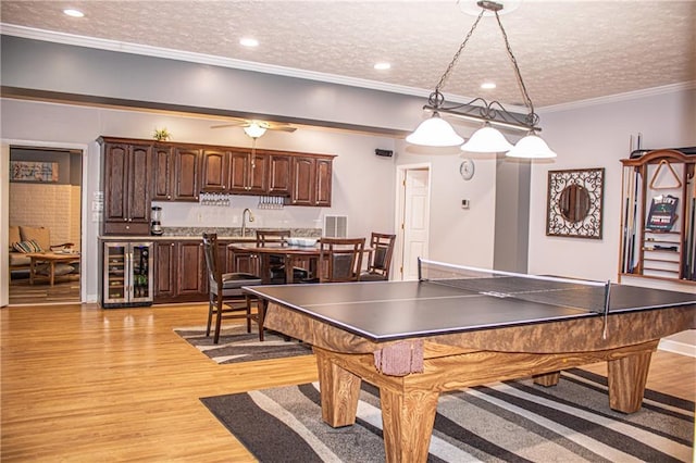 playroom with sink, light hardwood / wood-style flooring, ornamental molding, a textured ceiling, and beverage cooler