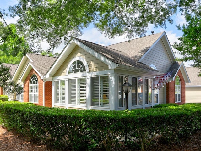 view of side of home featuring roof with shingles, a sunroom, and brick siding
