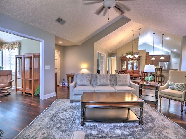 living area featuring wood finished floors, ceiling fan with notable chandelier, a textured ceiling, visible vents, and vaulted ceiling
