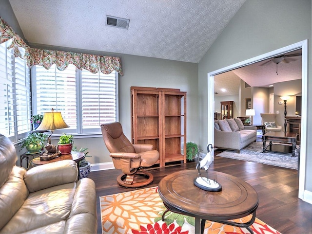 living area featuring vaulted ceiling, a textured ceiling, baseboards, visible vents, and wood finished floors