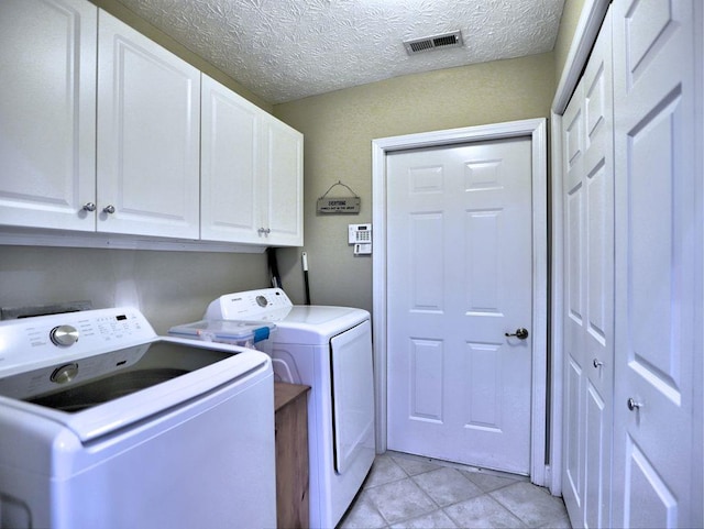 clothes washing area featuring a textured ceiling, light tile patterned floors, visible vents, washing machine and clothes dryer, and cabinet space