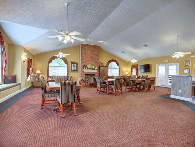 carpeted dining room with visible vents, vaulted ceiling, a brick fireplace, a ceiling fan, and baseboards