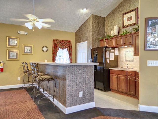kitchen featuring a peninsula, black fridge, a kitchen breakfast bar, ceiling fan, and vaulted ceiling