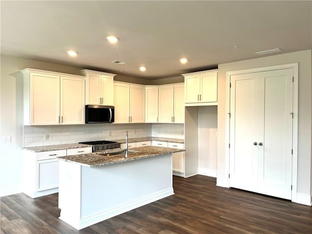 1059 Crest Mill Dr, Marietta, GA 30008 - kitchen with stainless steel microwave, dark wood-style flooring, stone countertops, decorative backsplash, and an island with sink