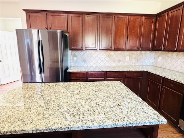 kitchen with tasteful backsplash, light stone countertops, and stainless steel fridge