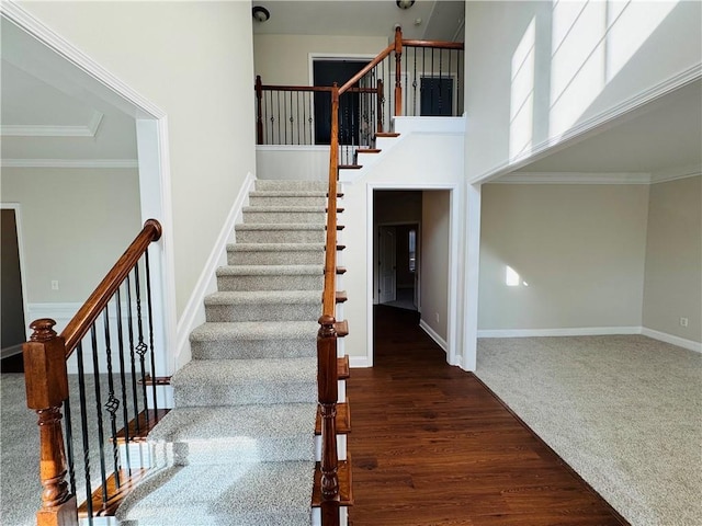 stairs featuring wood-type flooring, ornamental molding, and a high ceiling