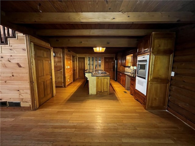 kitchen with beamed ceiling, light hardwood / wood-style floors, wooden walls, and sink