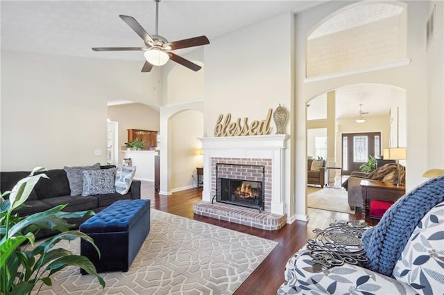 living room with visible vents, high vaulted ceiling, wood finished floors, arched walkways, and a brick fireplace