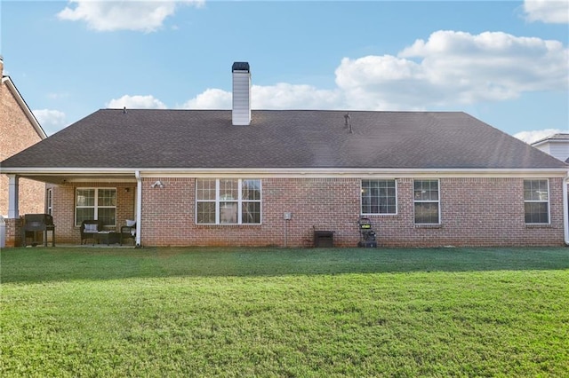 back of property with a yard, brick siding, a chimney, and a shingled roof