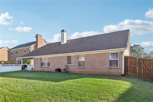 rear view of property with roof with shingles, a yard, a fenced backyard, a chimney, and brick siding