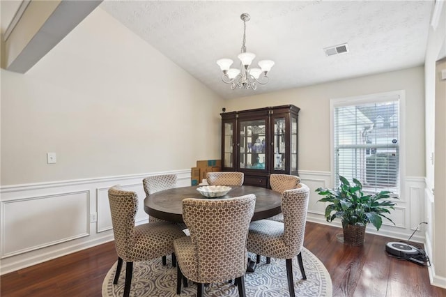 dining area featuring wood finished floors, a wainscoted wall, visible vents, a textured ceiling, and a chandelier