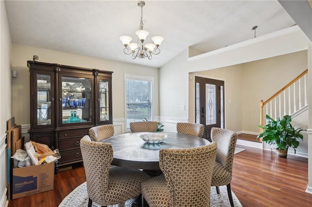 dining space featuring a wainscoted wall, dark wood-type flooring, a notable chandelier, lofted ceiling, and stairs