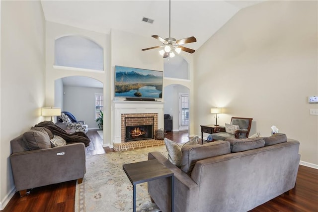 living area with dark wood-style floors, visible vents, a fireplace, and high vaulted ceiling