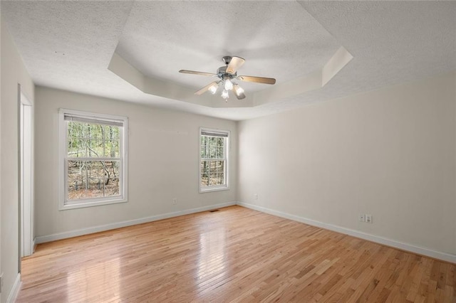 empty room featuring light wood-type flooring, a raised ceiling, a textured ceiling, and baseboards