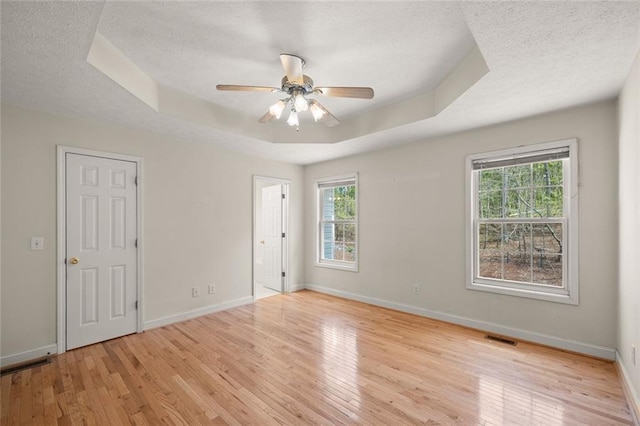 unfurnished room with a textured ceiling, visible vents, plenty of natural light, and a tray ceiling