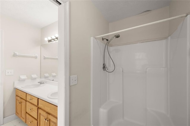 bathroom with double vanity, a sink, a textured ceiling, and walk in shower