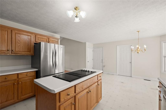 kitchen featuring an inviting chandelier, freestanding refrigerator, light floors, black electric cooktop, and brown cabinets