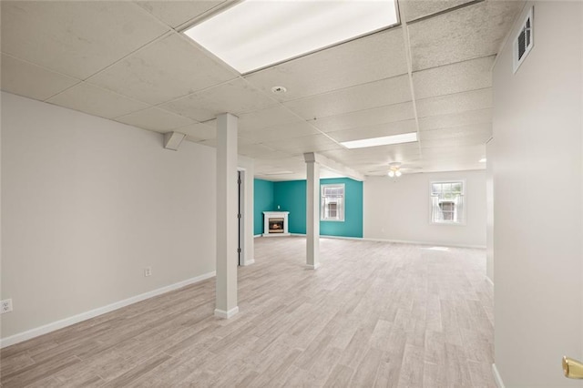 below grade area with light wood-type flooring, a paneled ceiling, and baseboards