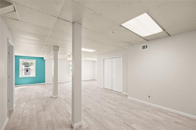 below grade area featuring baseboards, visible vents, a paneled ceiling, and light wood-style floors