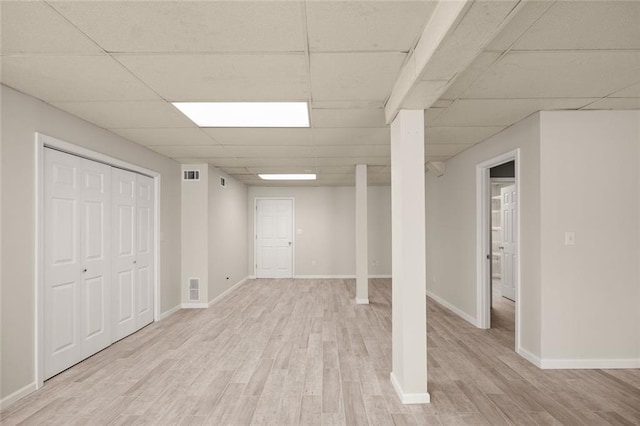 finished below grade area with light wood-style floors, a drop ceiling, and visible vents