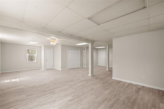 basement with baseboards, ceiling fan, light wood-style flooring, and a paneled ceiling