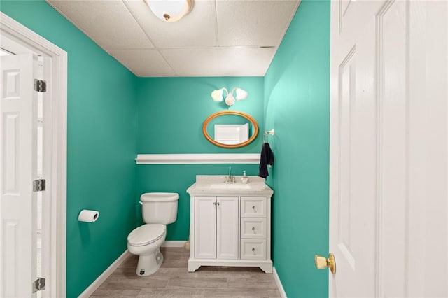 bathroom featuring vanity, wood finished floors, toilet, baseboards, and a drop ceiling