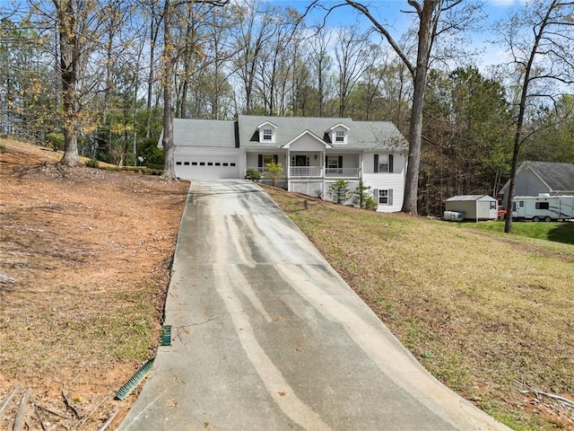 cape cod-style house featuring a front lawn, covered porch, driveway, an attached garage, and a storage shed